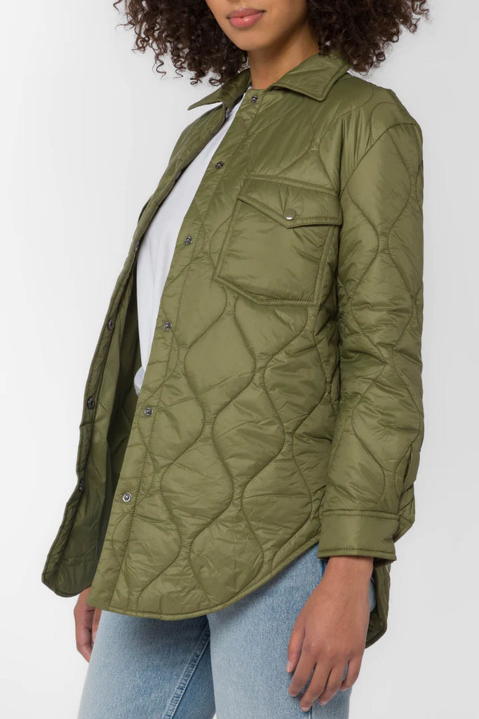 The Eleanor light weight puffer in olive color is crafted from a nylon quilted fabric. It features chest pockets, side seam pockets, snap closure and a dolphin hem for a flattering fit.