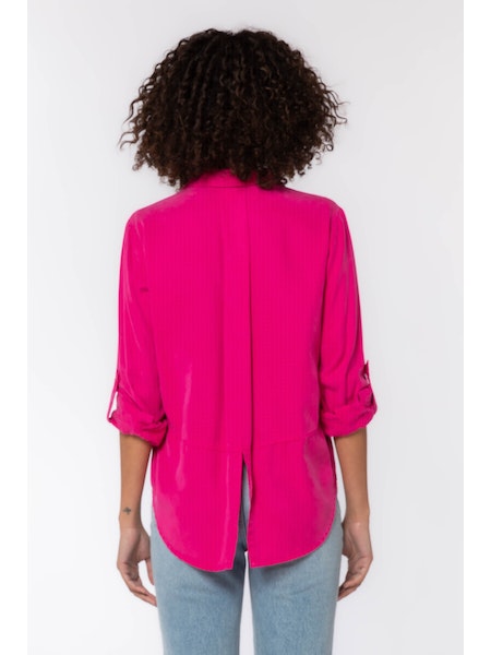 The Riley collared button-down shirt in Bright Fuchsia features rolled tab sleeves, double chest pockets, a split back tail, and a hi-lo hem. This shirt is a perfect staple to any wardrobe. 
