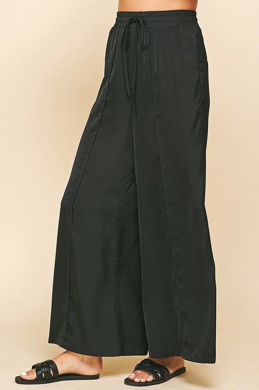 Satin Wide Leg Pants in black. Satin pants featuring a high-rise waist with hidden front pockets, jetted back pockets with a wide leg. Dress them up or down. Fabric Content: 100% POLYESTER