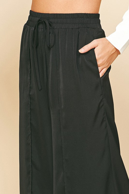 Satin Wide Leg Pants in black. Satin pants featuring a high-rise waist with hidden front pockets, jetted back pockets with a wide leg. Dress them up or down. Fabric Content: 100% POLYESTER